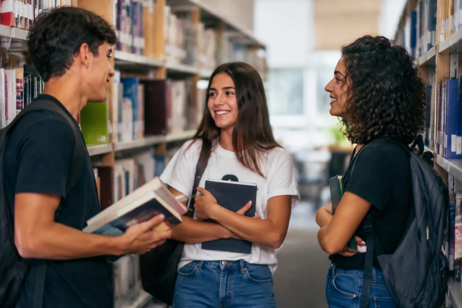 Estudantes conversando em pé entre as estantes de uma biblioteca